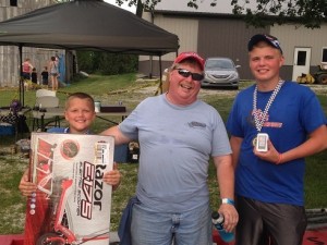 Team owner Jim Howe (center) celebrates twin podiums and some really nifty prizes with drivers Eli Fox (left) and Bransten Peavler at the 12th annual Goodland Grand Prix